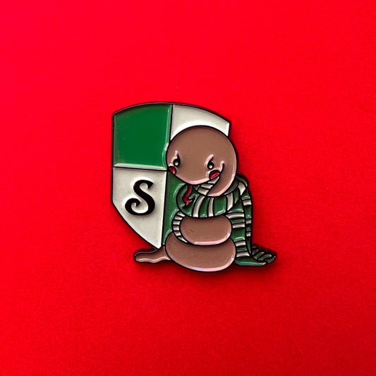 Pin de Slytherin con una serpiente tierna sobre el escudo de la casa, en tonos verdes y plateados.