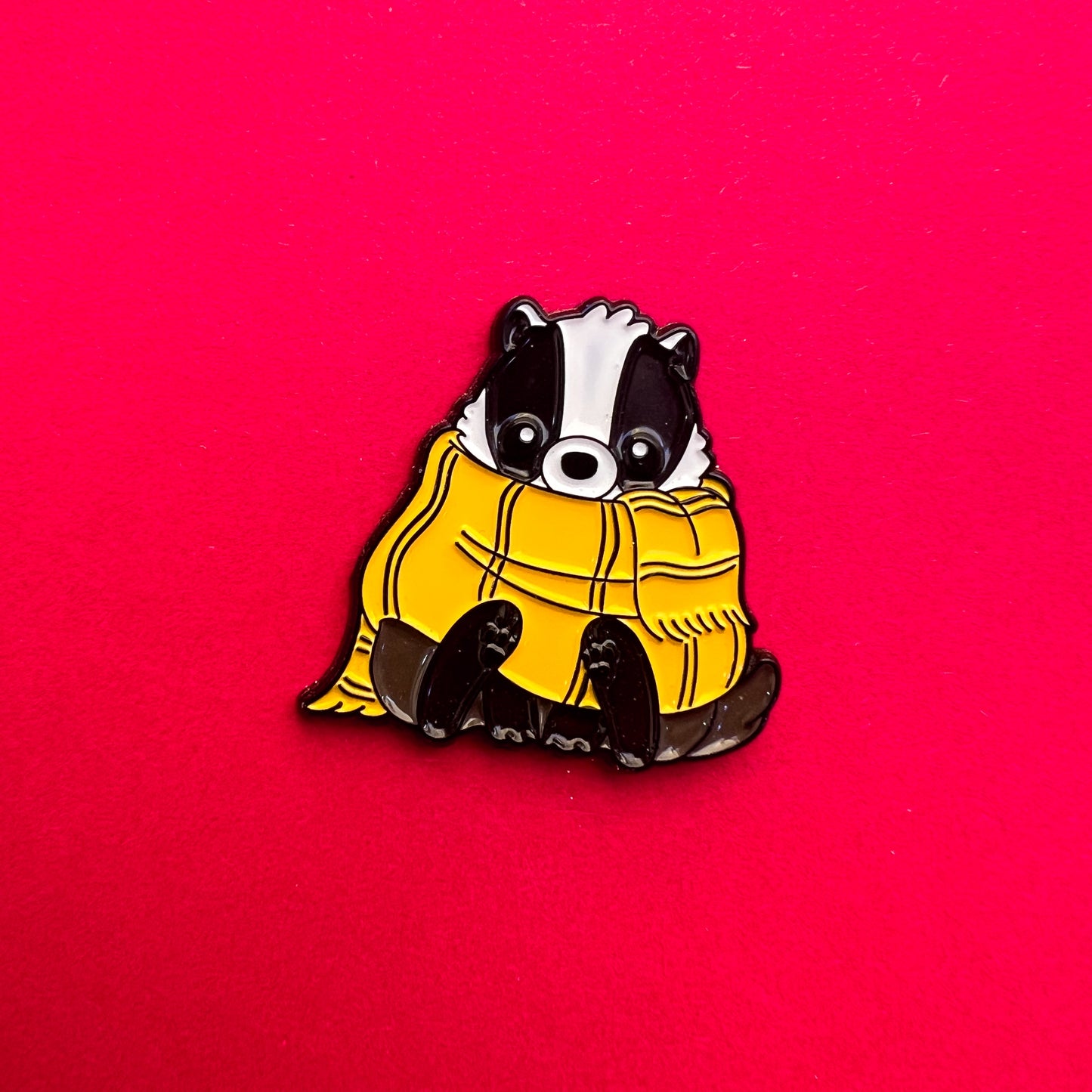 Pin de Hufflepuff: tejón tierno con bufanda amarilla y negra. ¡Ideal para leales y trabajadores!